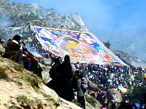 Photo of a large Tibetan tanka painting on a mountainside surrounded by Tibetans.